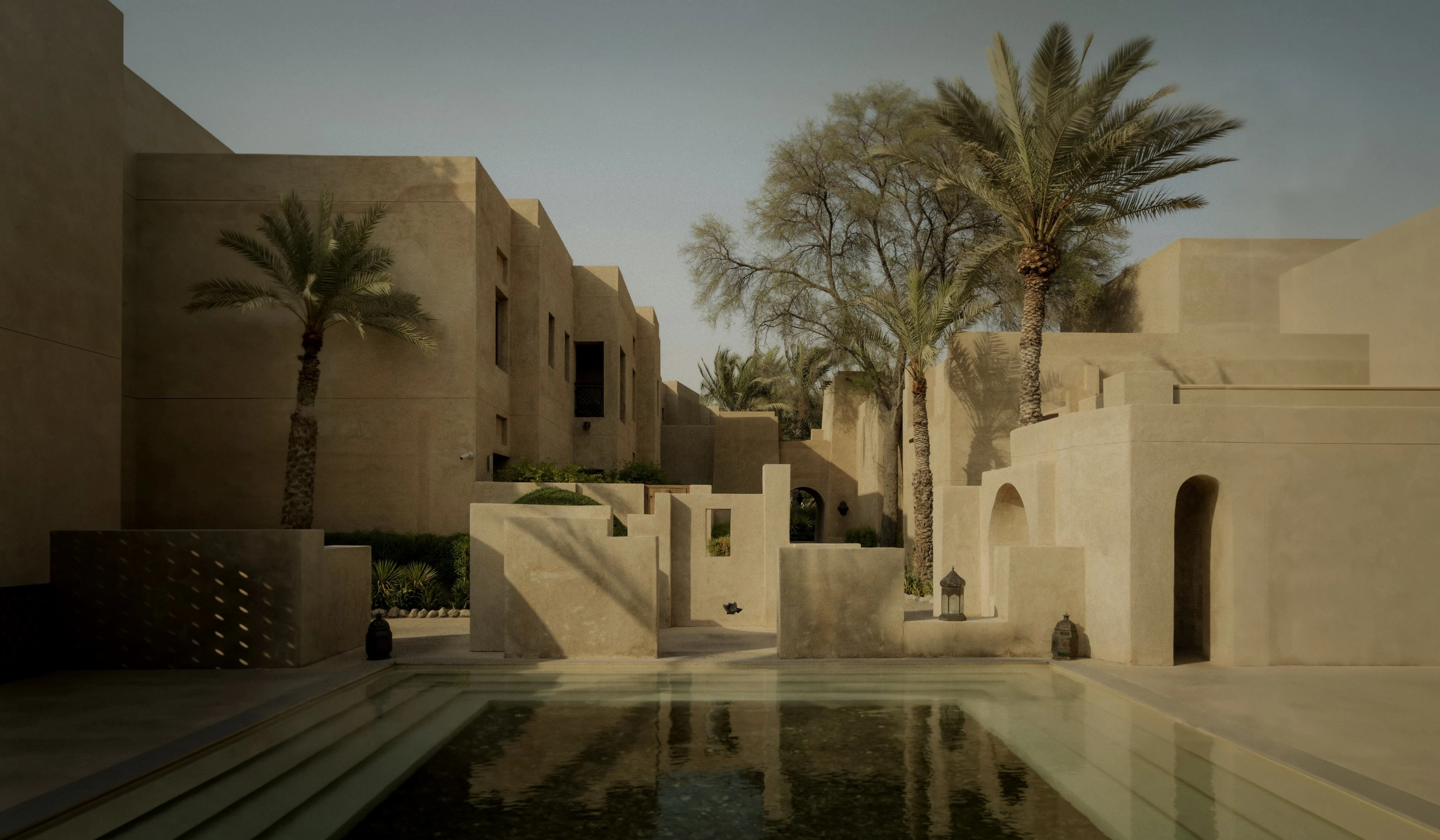 Sand-coloured courtyard with date palms and a still reflecting pool